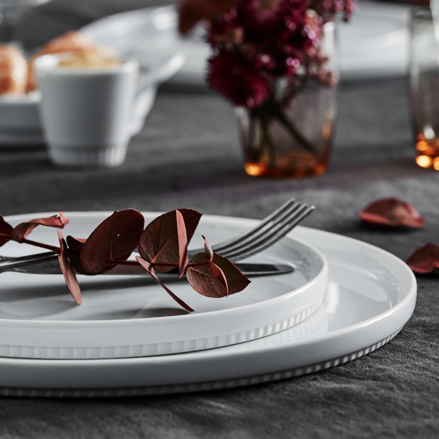 White ceramic plates with silverware on a dark tablecloth, with a blurred background of a meal setting.