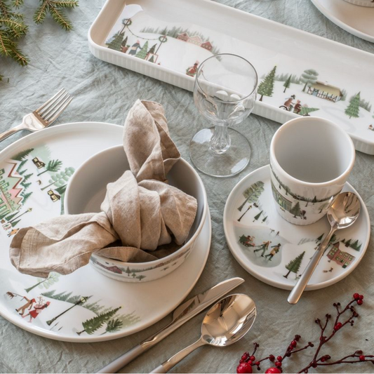 Christmas-themed table setting with decorative plates, cups, and cutlery on a gray tablecloth.