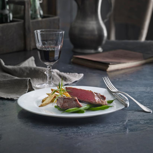 Plated dish of meat with vegetables on a dark table with a glass of red wine.