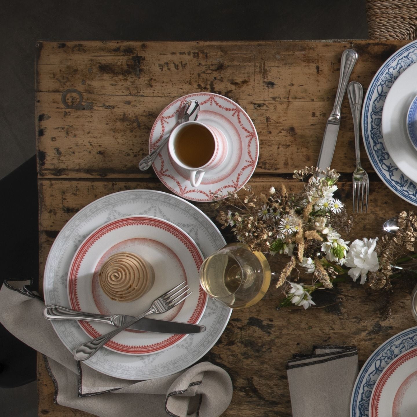 Dining table setting with plates, cups, and cutlery on a rustic wooden table.