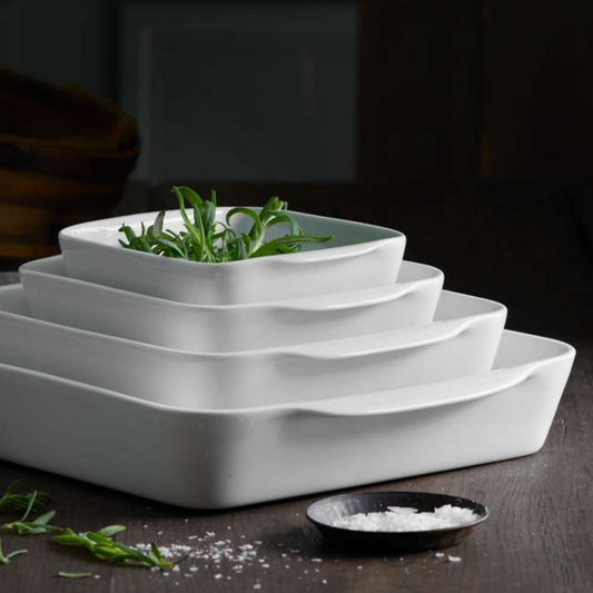 Set of white, wavy-patterned ceramic trays with greenery on a dark surface.