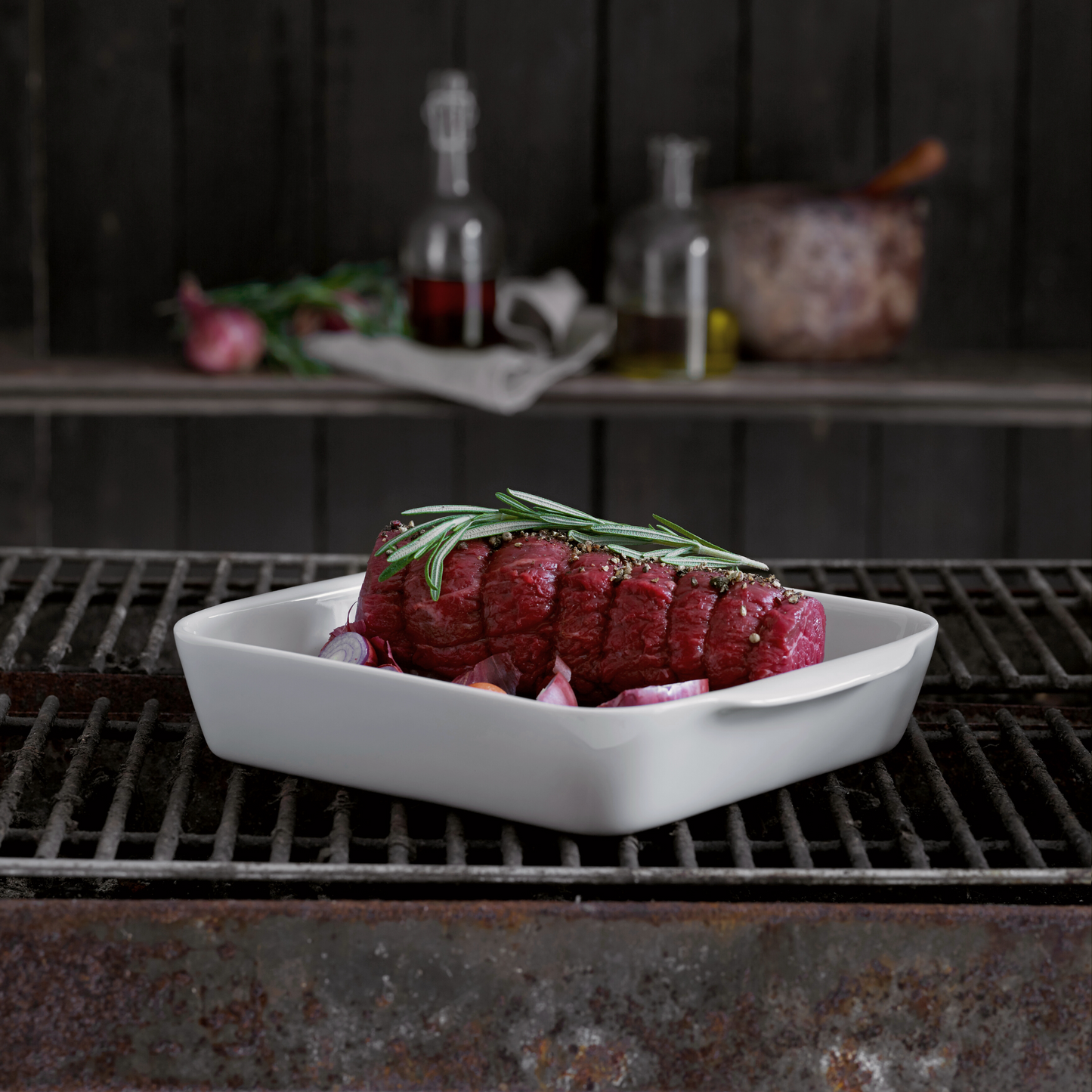 Raw steak with rosemary on a white plate over a grill
