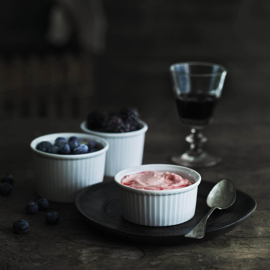 Three white ramekins with different desserts on a dark surface, accompanied by a glass of dark liquid.