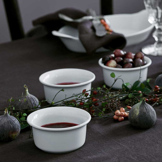 White ceramic bowls with red sauce on a dark tablecloth with figs and berries.