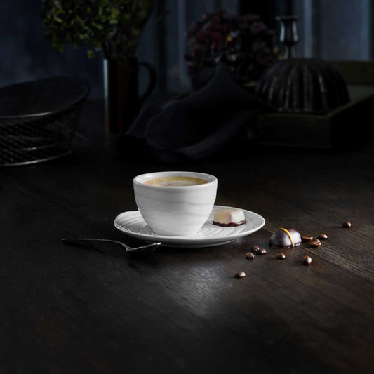 White coffee cup on a dark wooden table with scattered coffee beans and a spoon.