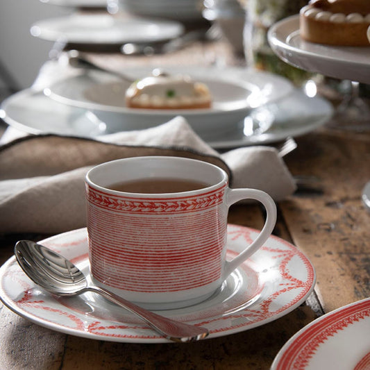 Teacup with red patterns on a saucer with a spoon, set on a wooden table.