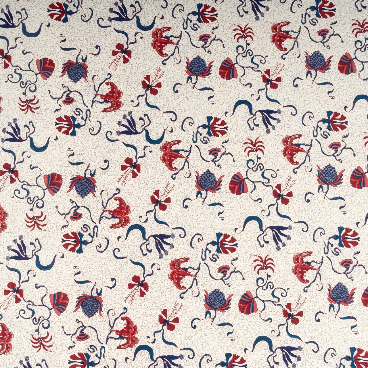 Patterned fabric with red, blue, and black floral and abstract designs on a beige background