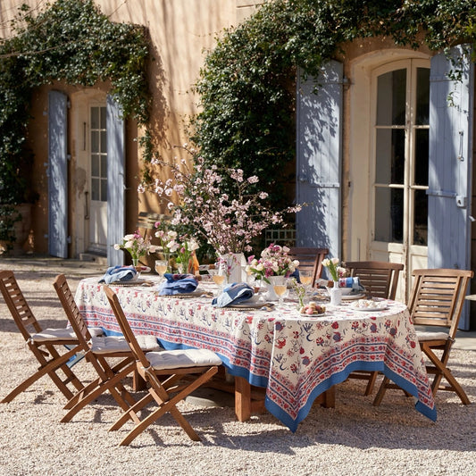 Outdoor dining setup with a floral tablecloth and chairs in front of a building with blue shutters.