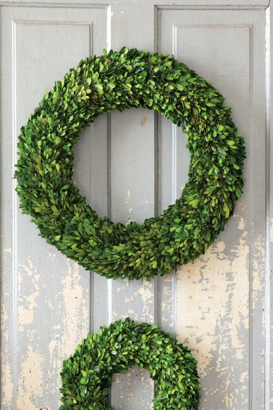 Two green boxwood wreaths on a textured gray door.