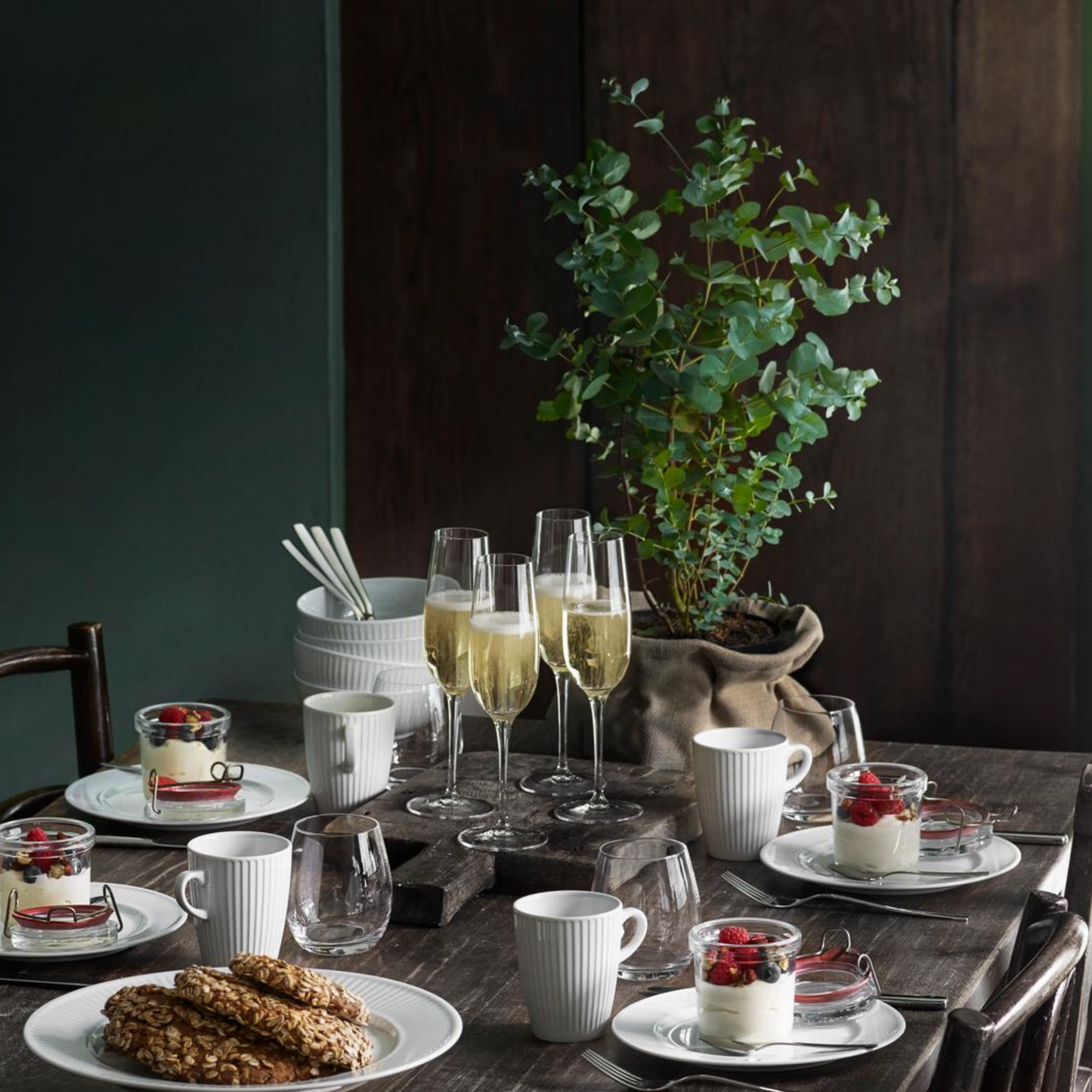 Dining table set with plates, glasses, and a plant in the background
