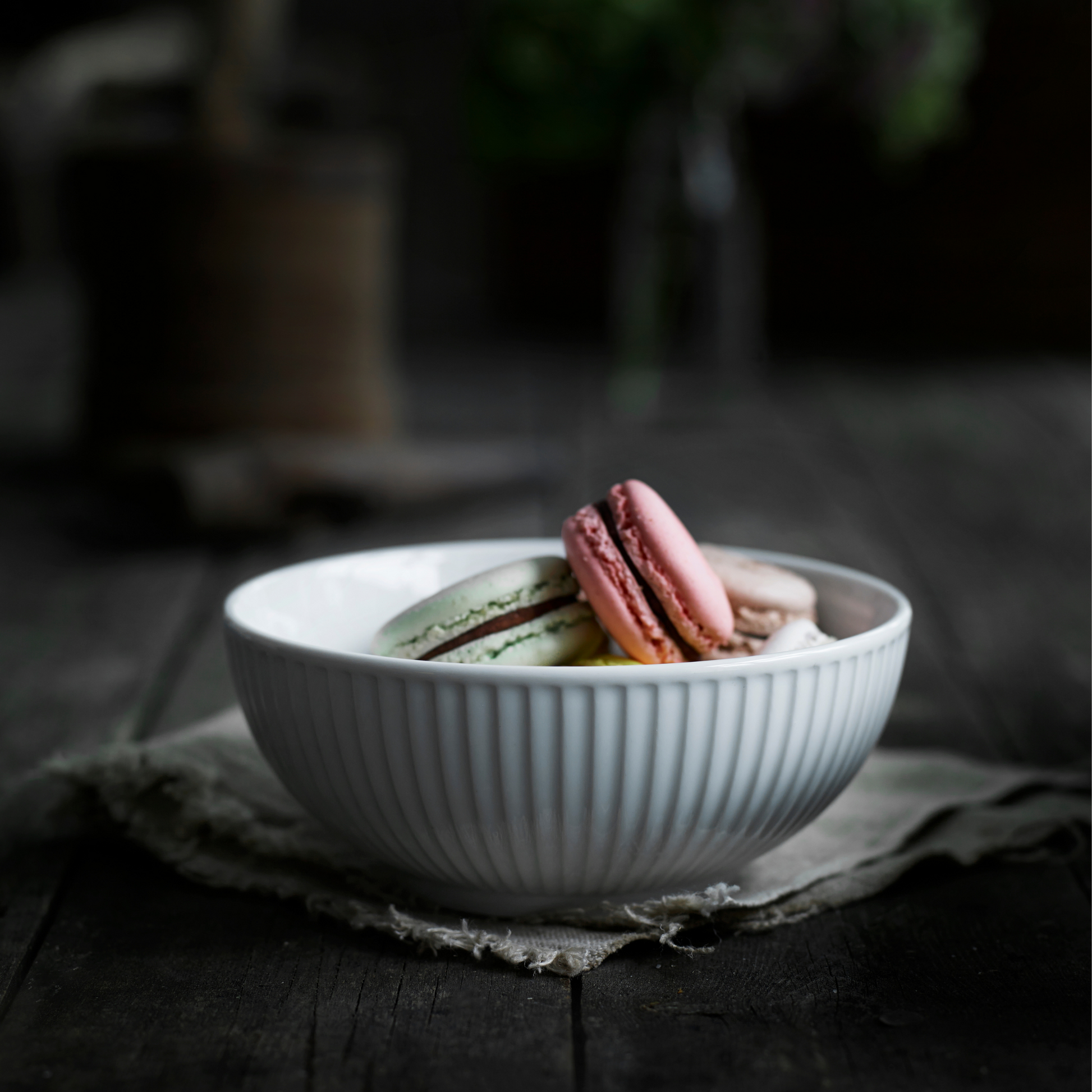 White bowl with colorful macarons on a dark wooden surface
