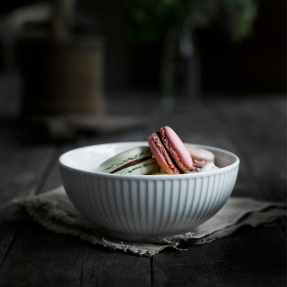 White bowl with colorful macarons on a dark wooden surface