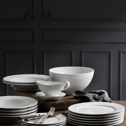 Set of white ceramic dinnerware on a wooden surface with a dark paneled wall background.