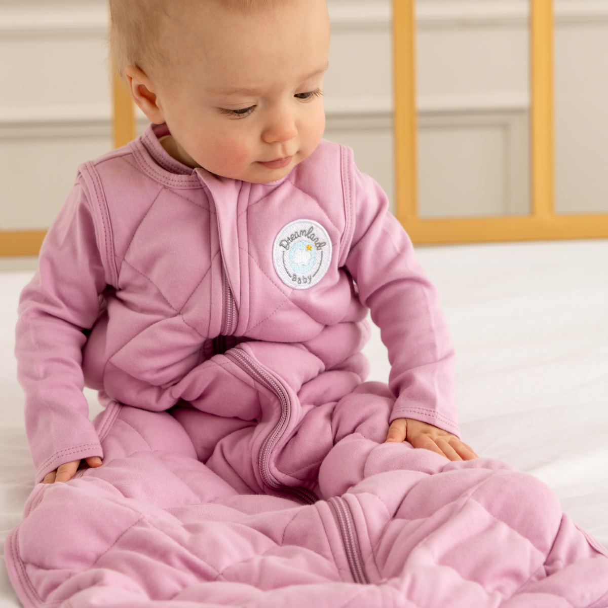 Baby wearing a pink quilted outfit with a visible brand logo, sitting on a white surface.