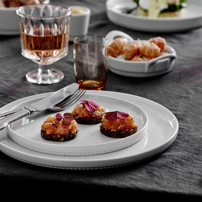 Dessert course with small dishes on a white plate, glasses of dessert wine, and a dark tablecloth.