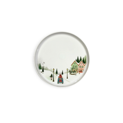 Round ceramic plate with a winter scene design featuring houses and trees on a white background