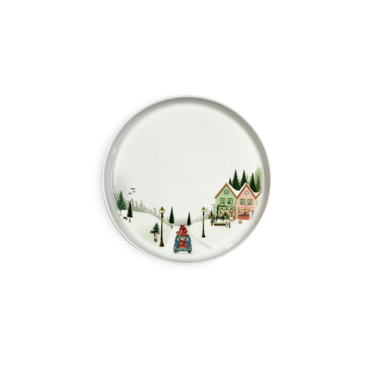 Round ceramic plate with a winter scene design featuring houses and trees on a white background
