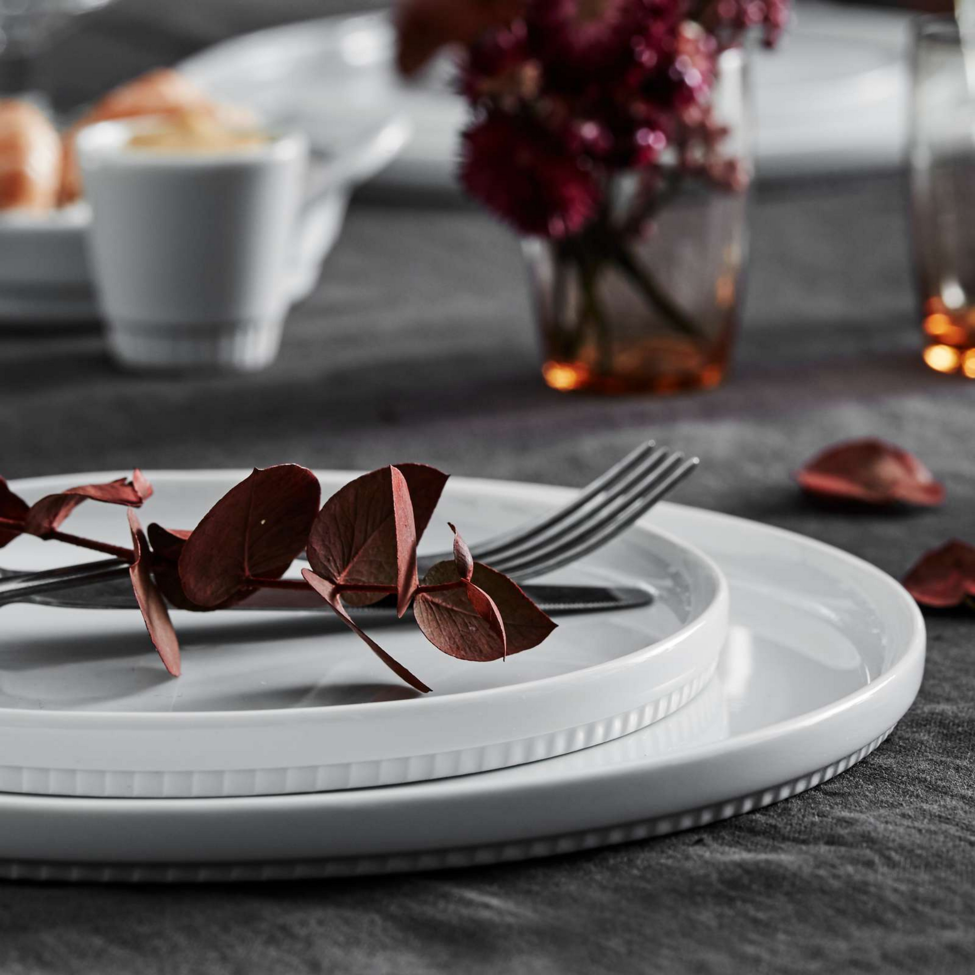 White ceramic plates with silverware on a dark tablecloth, with a blurred background of a meal setting.