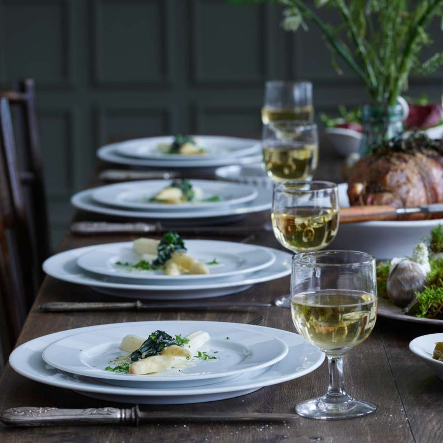 Dining table set with plates of food and glasses of white wine.