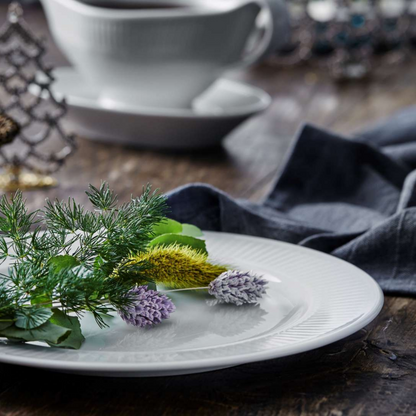 White plate with greenery and flowers on a wooden table with a blurred background