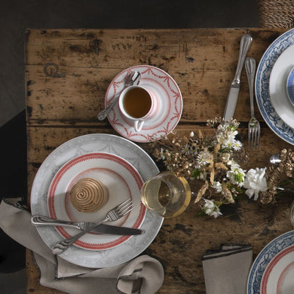 Dining table setting with plates, cups, and cutlery on a rustic wooden table.