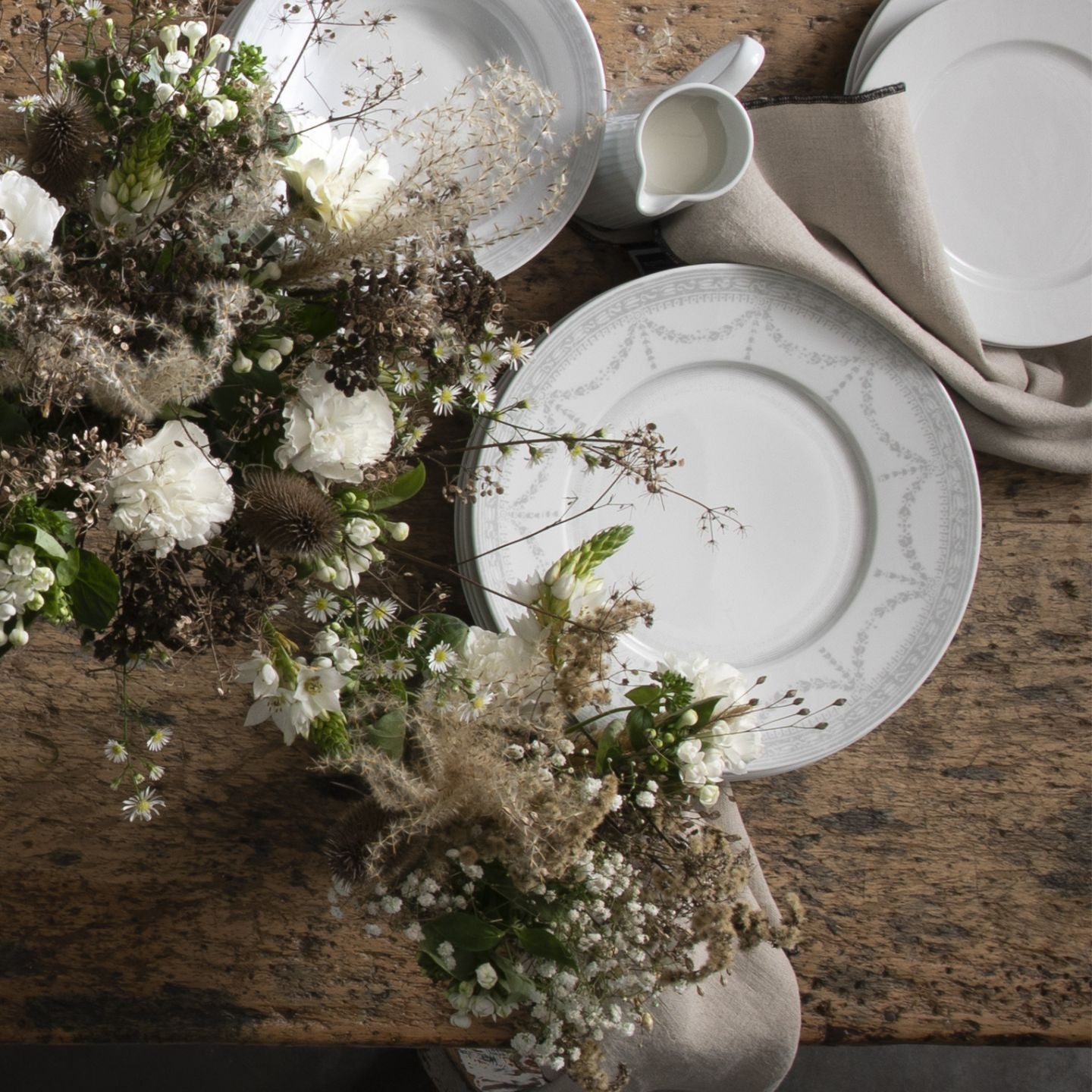 Table setting with white plates, flowers, and a pitcher on a wooden surface