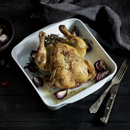 Roasted chicken on a white plate with onions and herbs on a dark surface