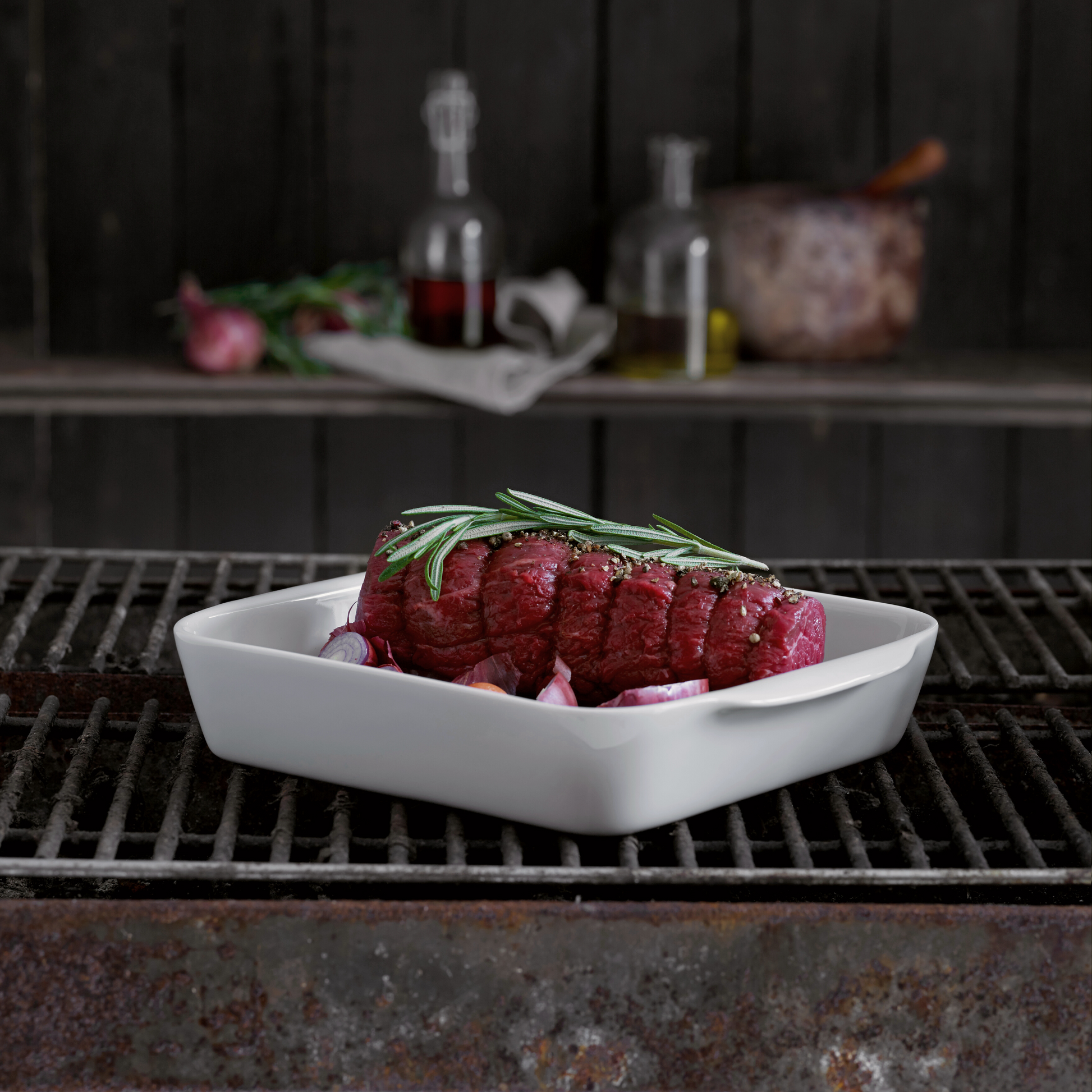 Raw steak with rosemary on a white plate over a grill