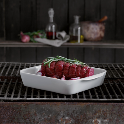Raw steak with rosemary on a white plate over a grill