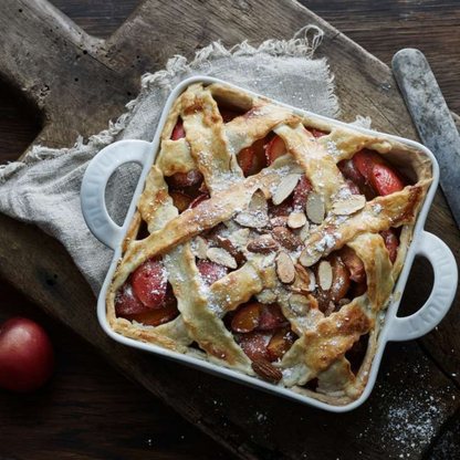 Baked pie with lattice crust in a white dish on a wooden surface
