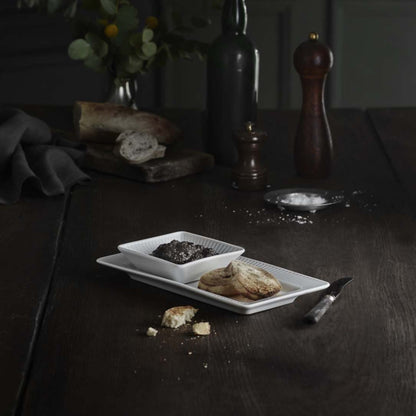 Dark wooden table with a white dish of food, bread, and a pepper grinder.