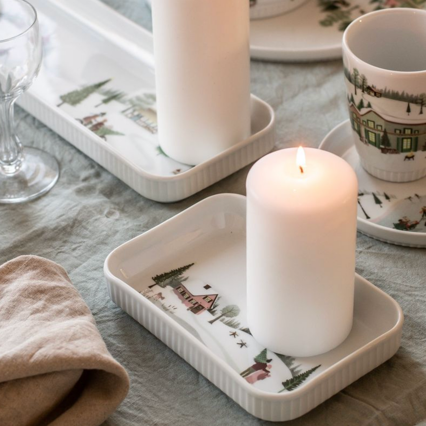 Candle on a decorative tray with a Christmas-themed design on a tablecloth.