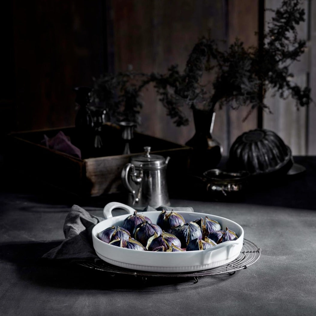 White oval dish with figs on a dark surface with a blurred background