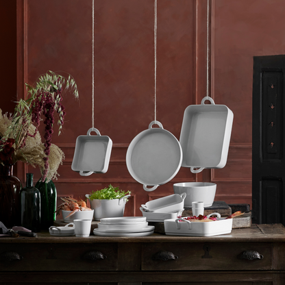 Set of white ceramic cookware on a wooden table with a dark red wall background