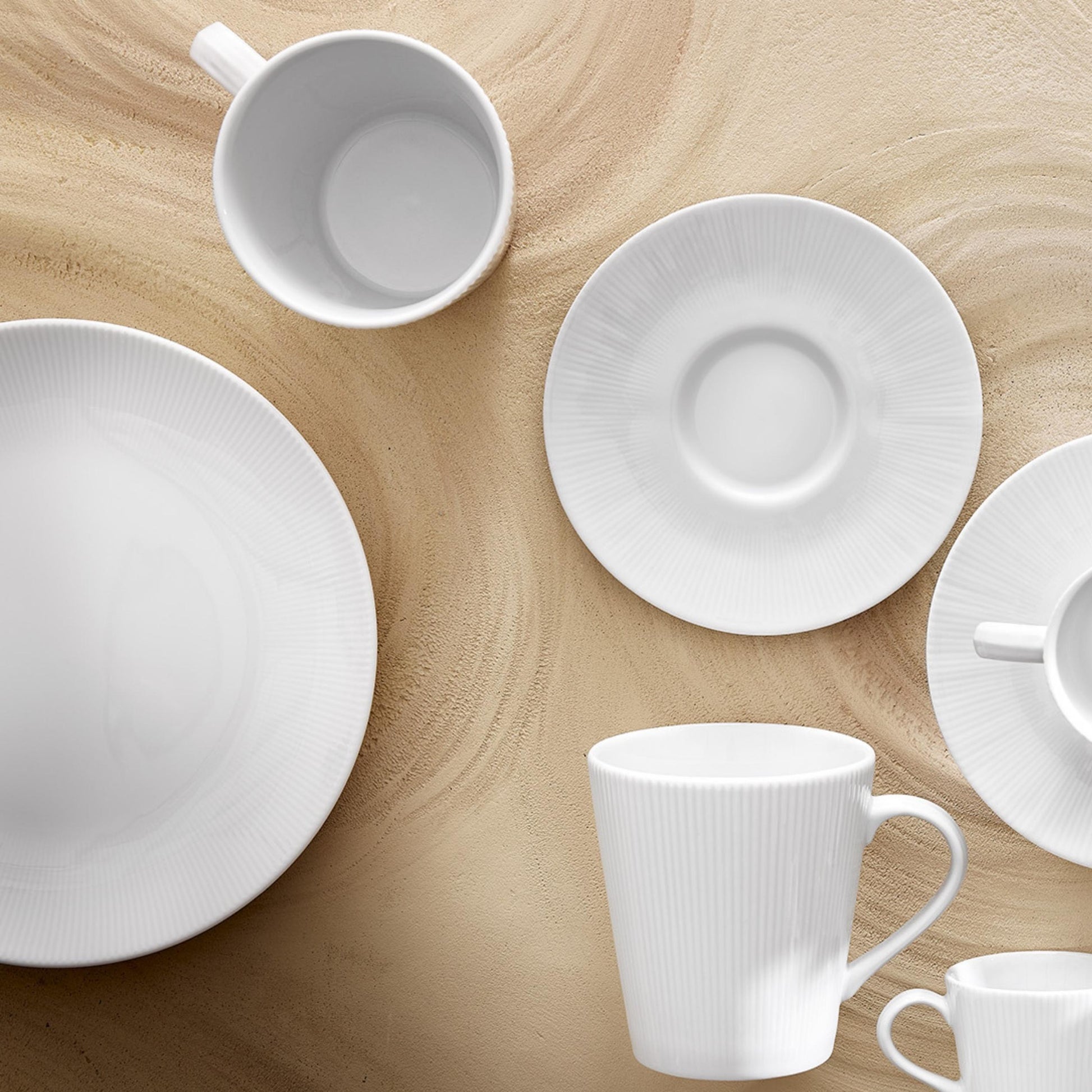 Set of white ceramic plates and mugs on a wooden surface