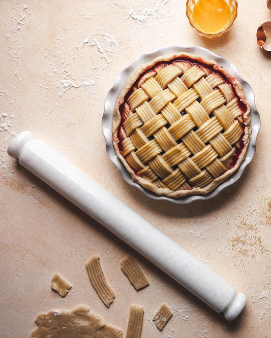 Baked pie with lattice crust on a floured surface next to a rolling pin and pastry scraps.