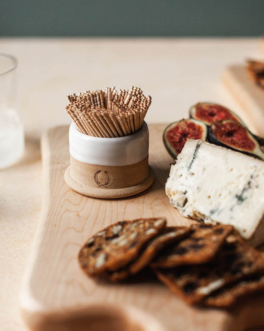 Bowl with toothpicks on a wooden board with cheese and figs