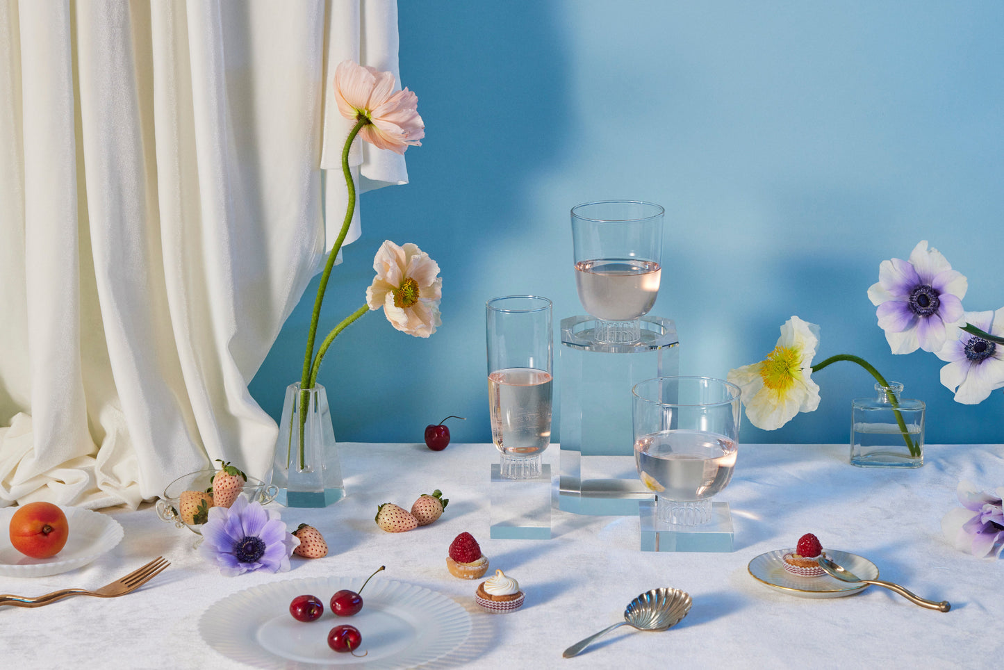 Table setting with flowers, glasses, and small plates on a white tablecloth against a blue wall.