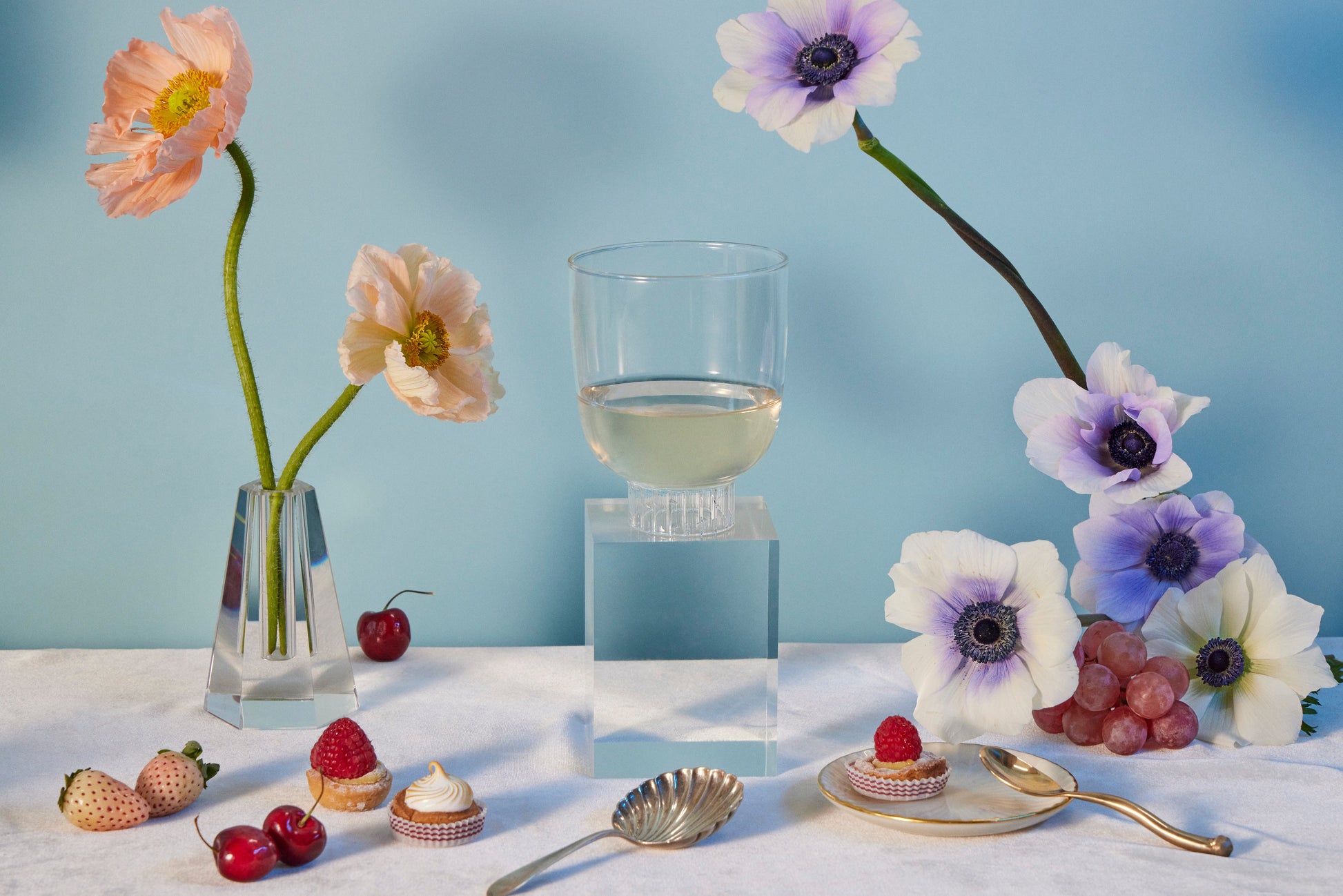 Table setting with flowers, glass of white wine, and small desserts against a light blue background