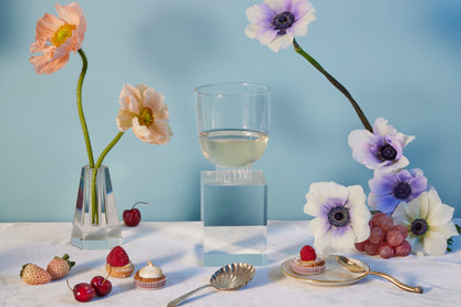 Table setting with flowers, glass of white wine, and small desserts against a light blue background