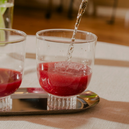 Red liquid being poured into a glass on a wooden table.