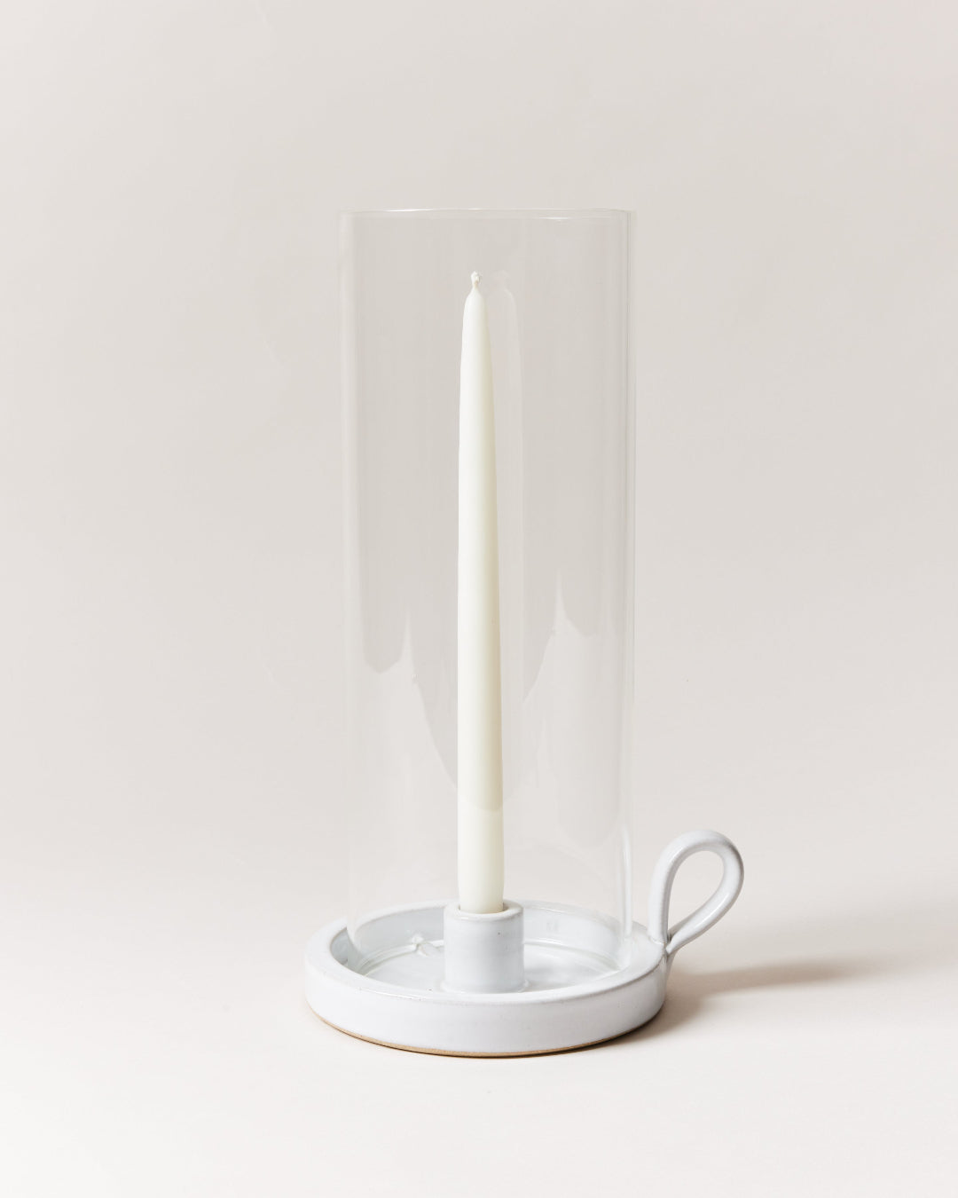 White candle in a glass holder on a white surface with a white background