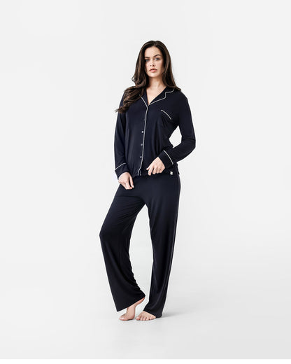 Woman wearing a black pajama set with white piping on a white background