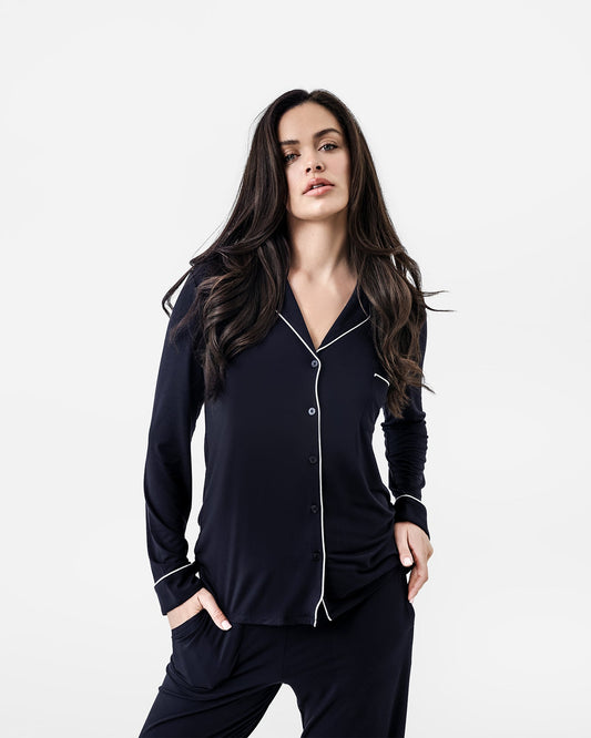 Woman wearing a black pajama set with white piping on a white background