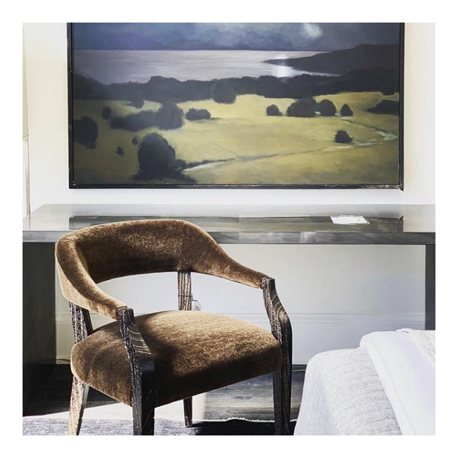 Brown armchair in a room with a large landscape painting on the wall.