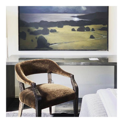 Brown armchair in a room with a large landscape painting on the wall.