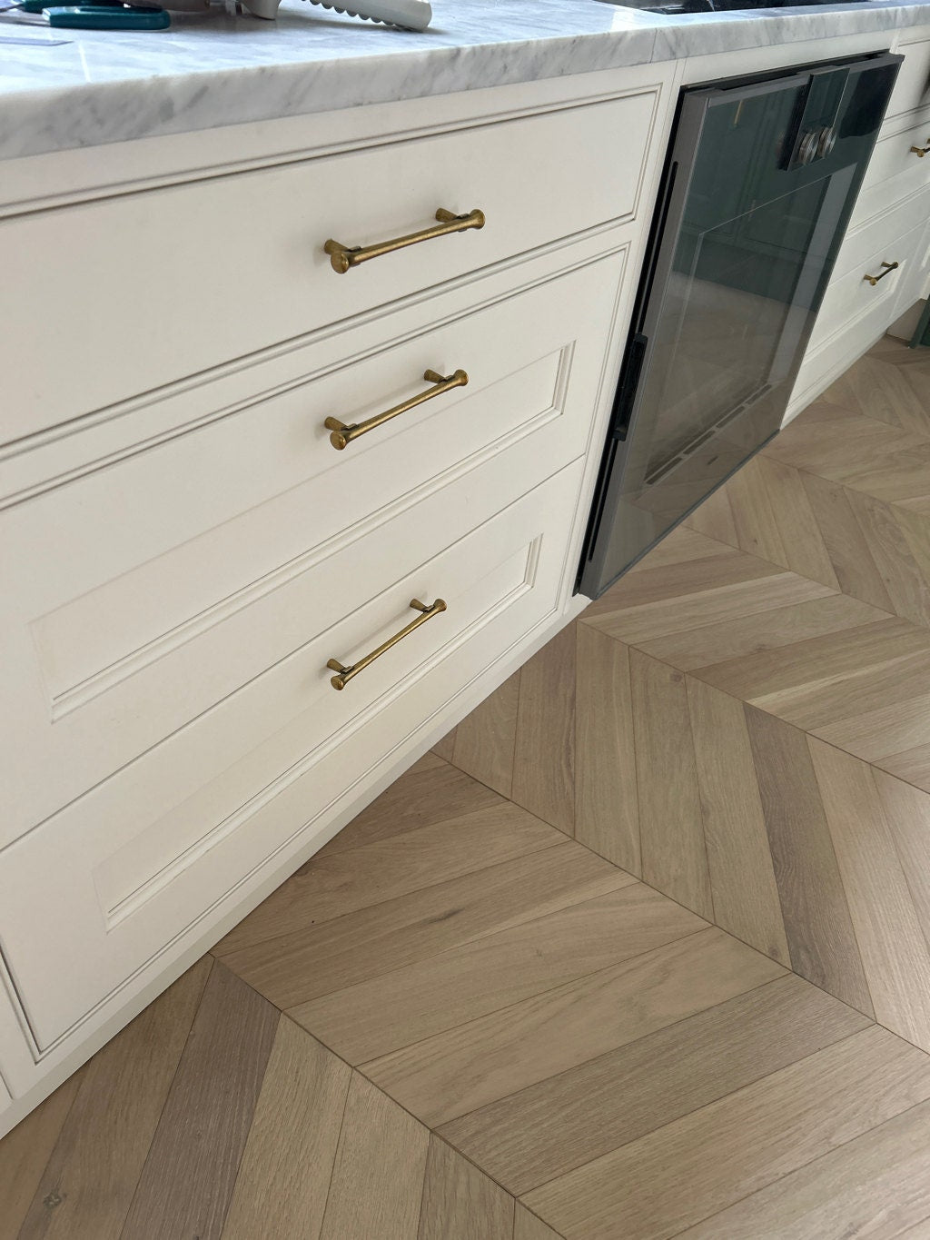 Kitchen with white cabinets, gold handles, and a herringbone wood floor.