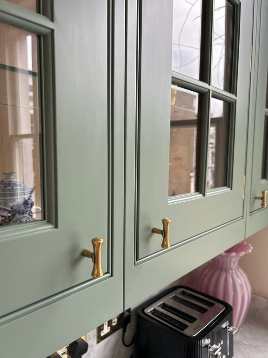Green cabinet with gold handles and a pink vase in the background