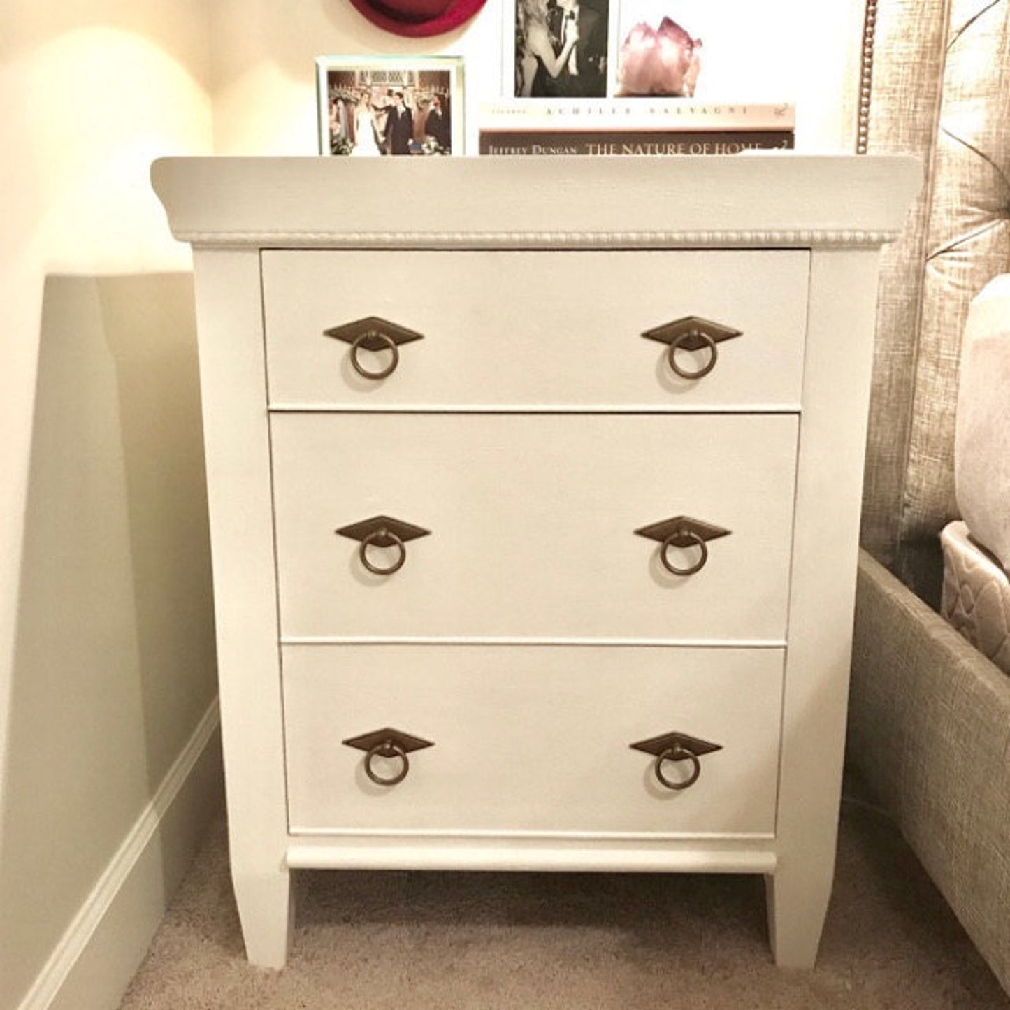 White nightstand with four drawers and metal ring handles in a bedroom setting.