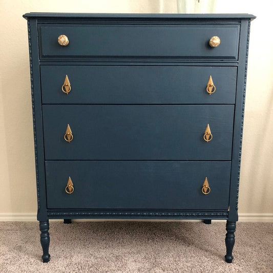 Blue dresser with gold knobs on a beige carpet and wall.